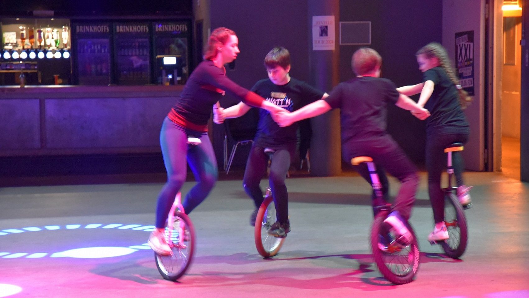 You can see a group of young people on unicycles. They are riding in a circle.