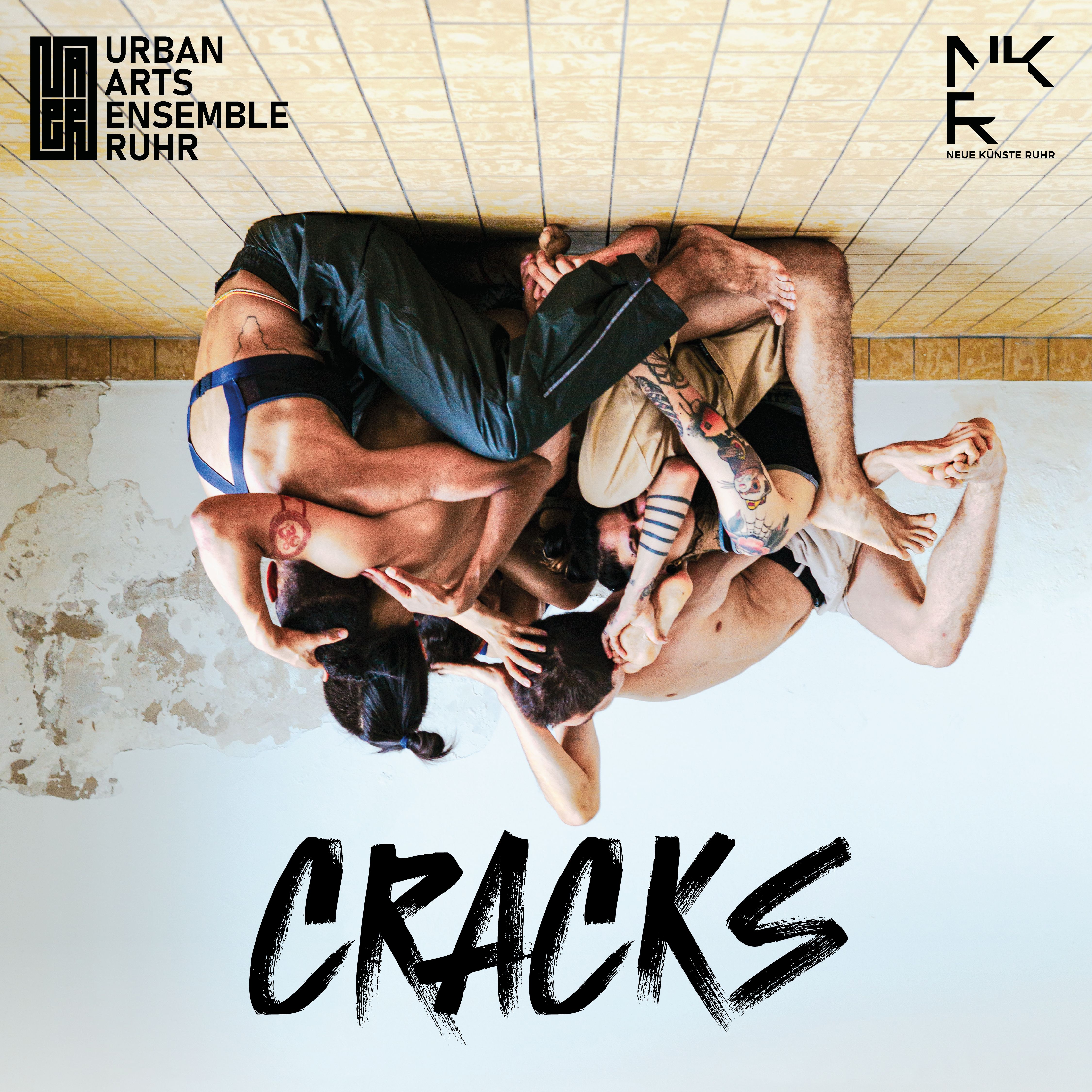 The photo shows dancers sitting on the floor and interlocked with each other. Underneath is the title CRACKS. 