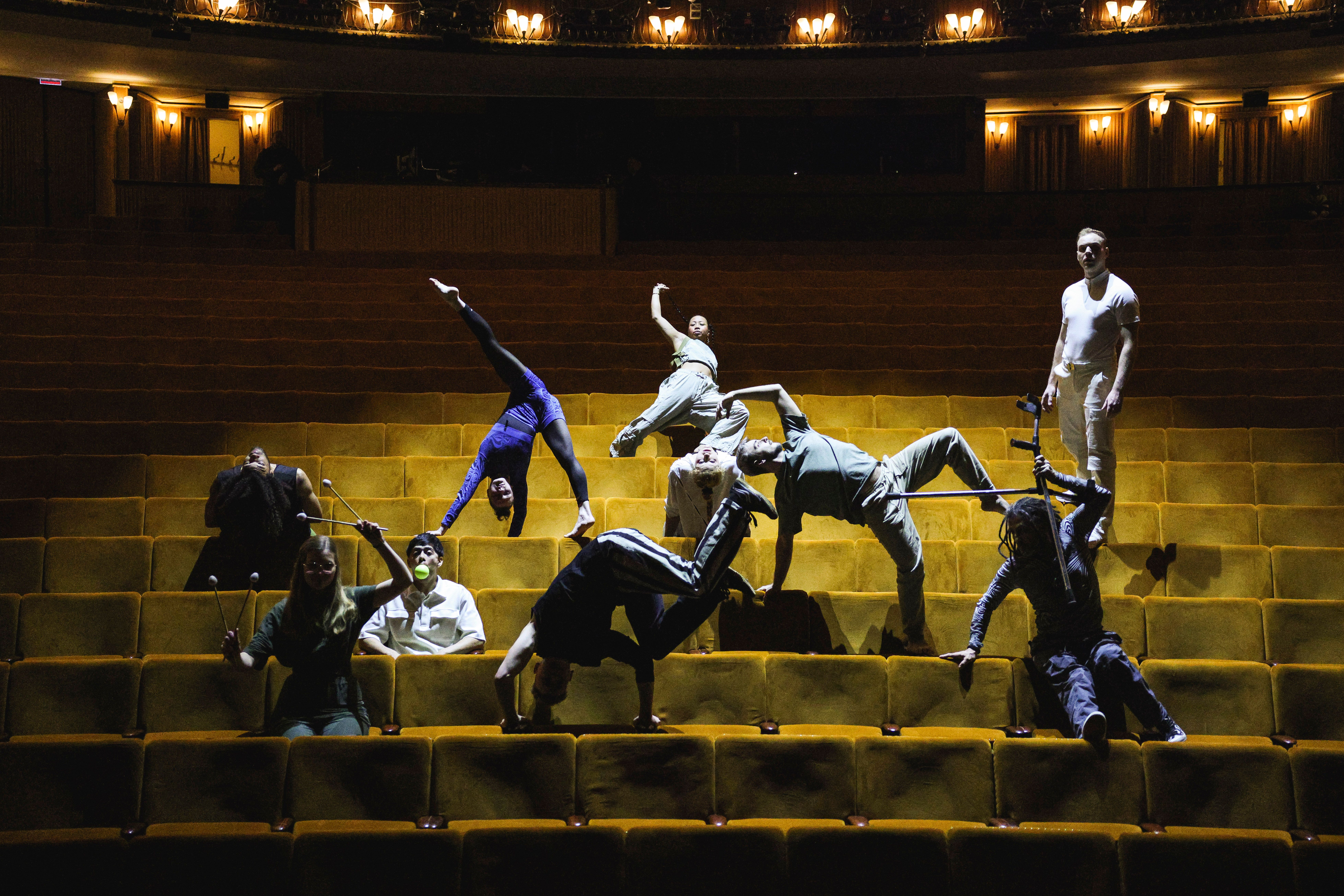 A group of people can be seen. They stand and sit in different poses in the auditorium of a theater.