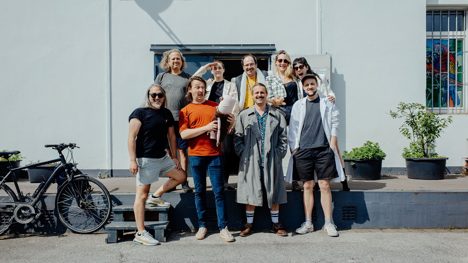 The picture shows nine people standing in front of a white, industrial building.