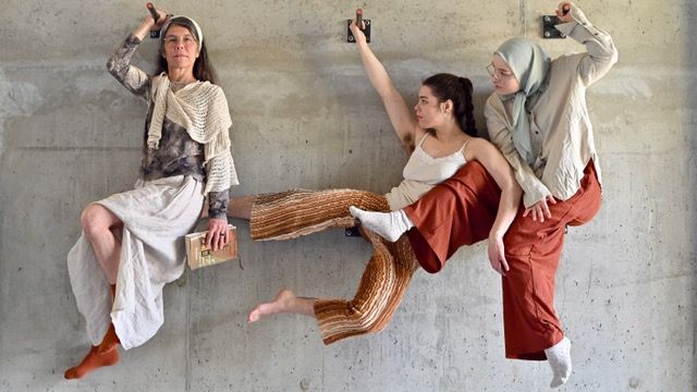 Two acrobats look at a speaker holding a book in her hand