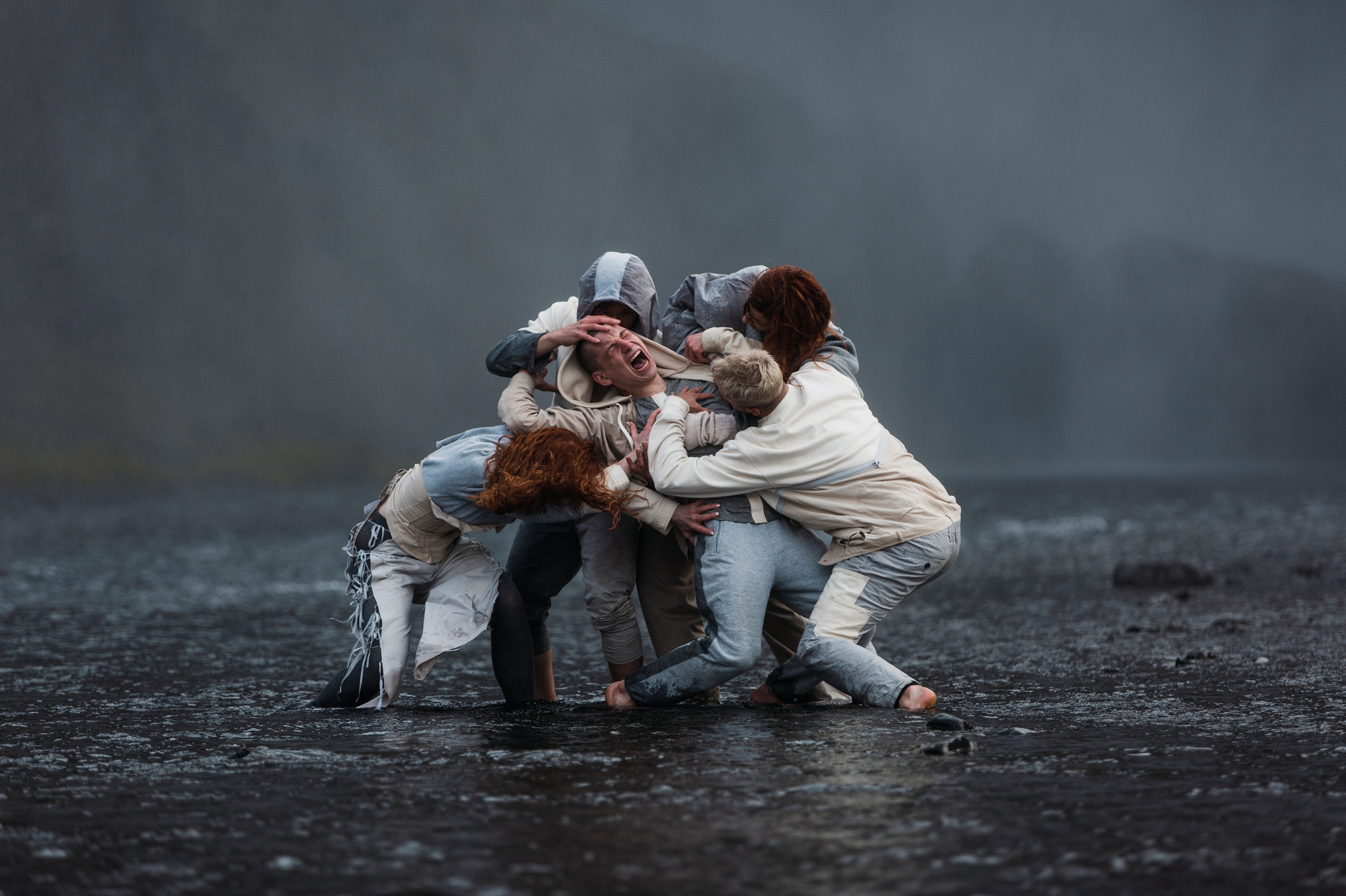 You can see a group of people. They are interlocked and are tearing at the person in the middle. The person in the middle has their eyes closed and their mouth wide open.