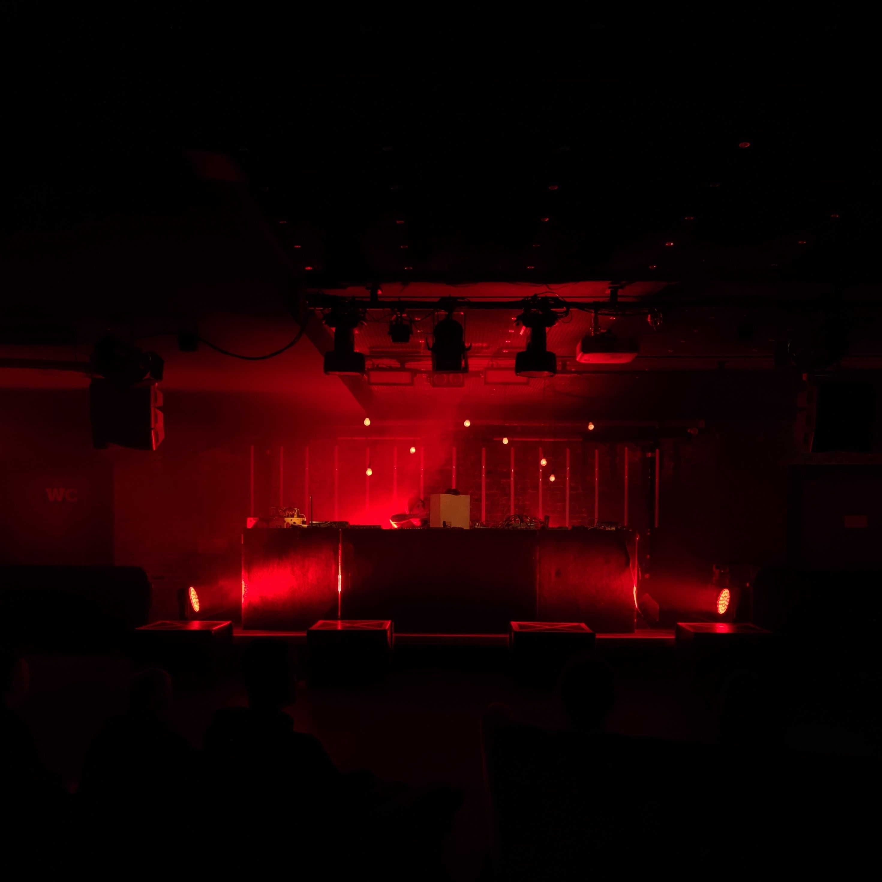 There is a stage and a DJ booth on the stage. The room is bathed in a red light.