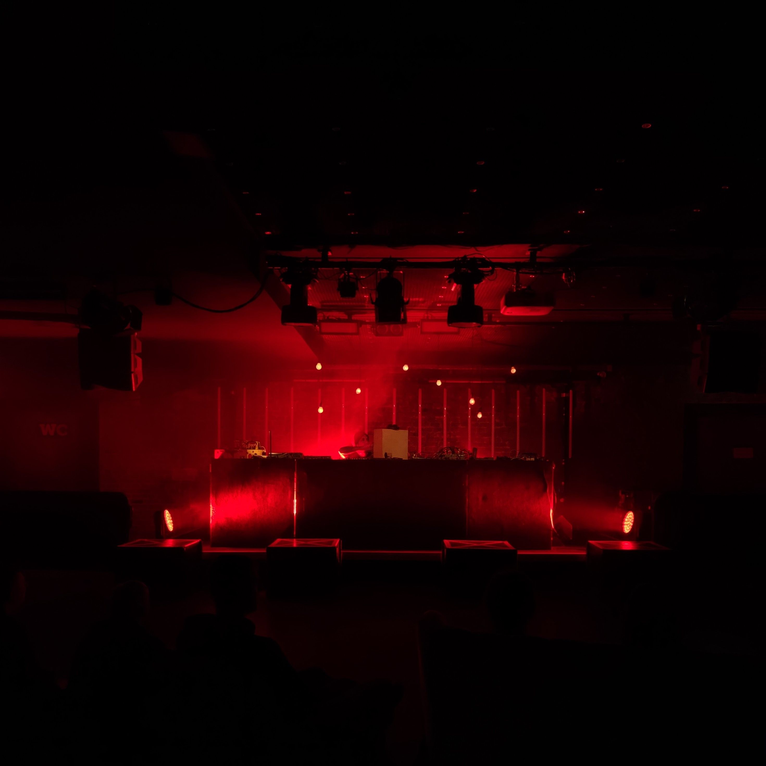There is a stage and a DJ booth on the stage. The room is bathed in a red light.