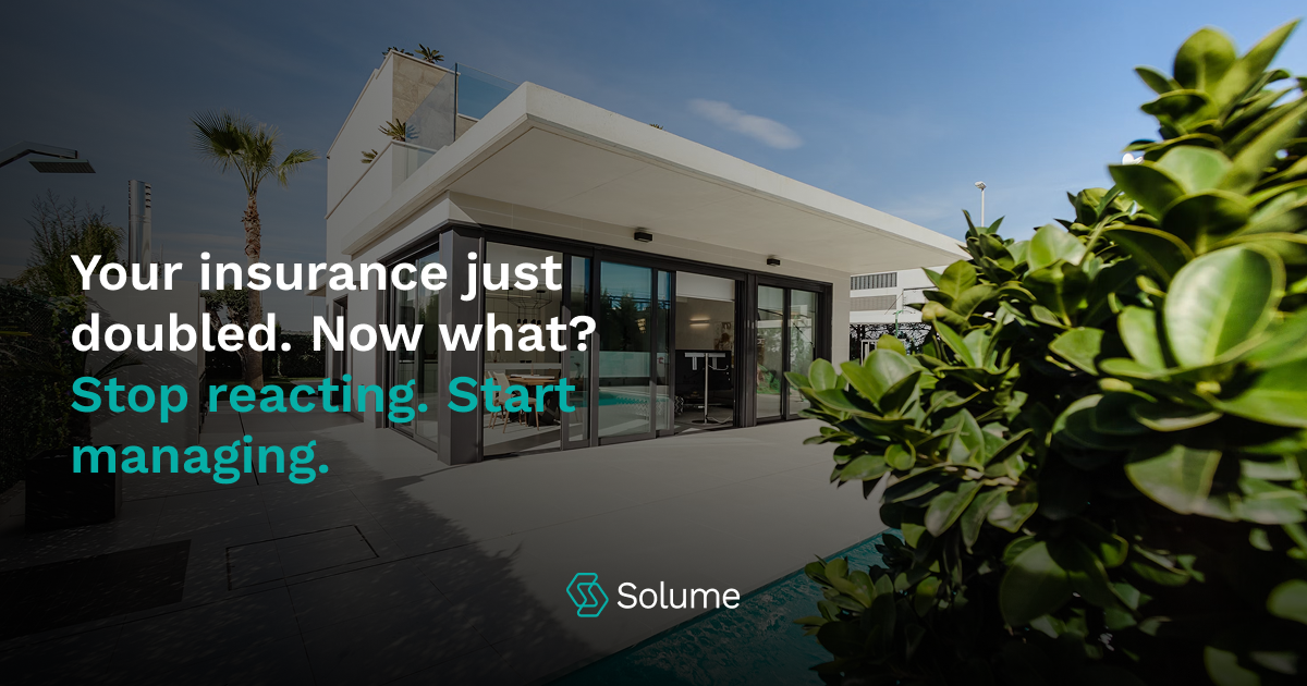 Modern condo building under clear blue sky with palm trees and lush landscaping. Bold headline text reads: “Your insurance just doubled. Now what?” followed by the sub headline: “Stop reacting. Start managing.” Includes Solume logo at the bottom.