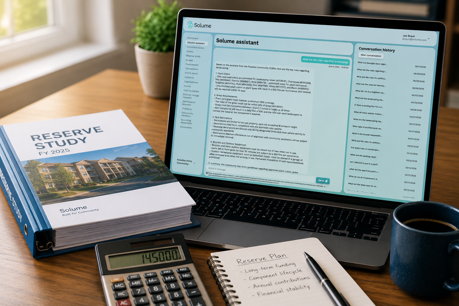 Close-up of a financial planning workspace featuring a reserve study binder, calculator, notebook, and coffee beside a laptop displaying the Solume Assistant dashboard for HOA reserve planning and community management.
