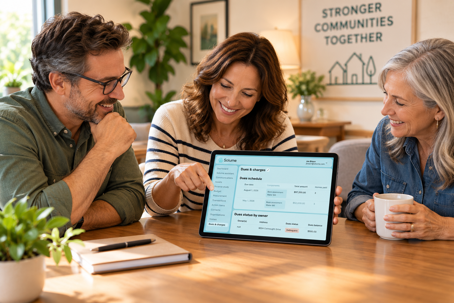 Three HOA board members smiling and reviewing the Solume dues and charges dashboard on a tablet during a relaxed meeting in a bright, modern office.