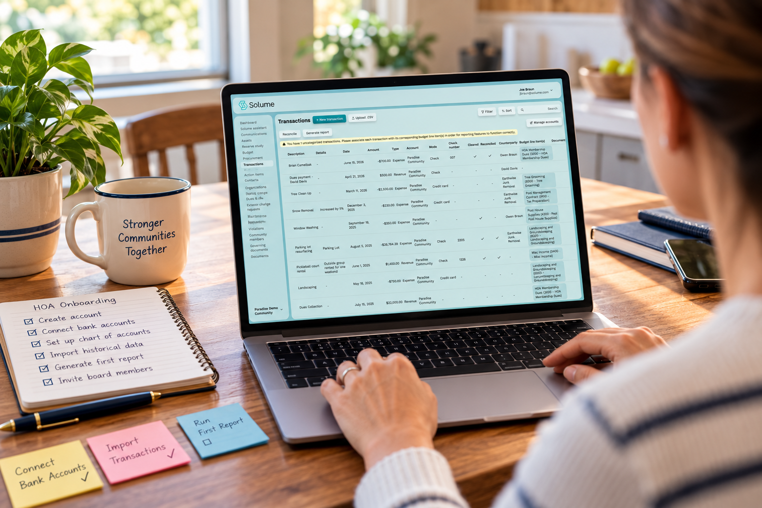 HOA treasurer using a laptop to access Solume’s transaction management dashboard, reviewing financial records, payments, and reconciliation details at a kitchen table.