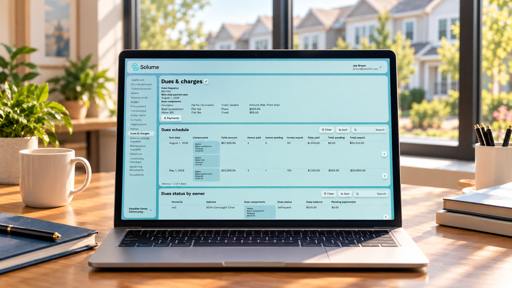 Solume HOA dues and charges dashboard displayed on a laptop in a bright clubhouse office, showing payment schedules, dues balances, and owner payment statuses.