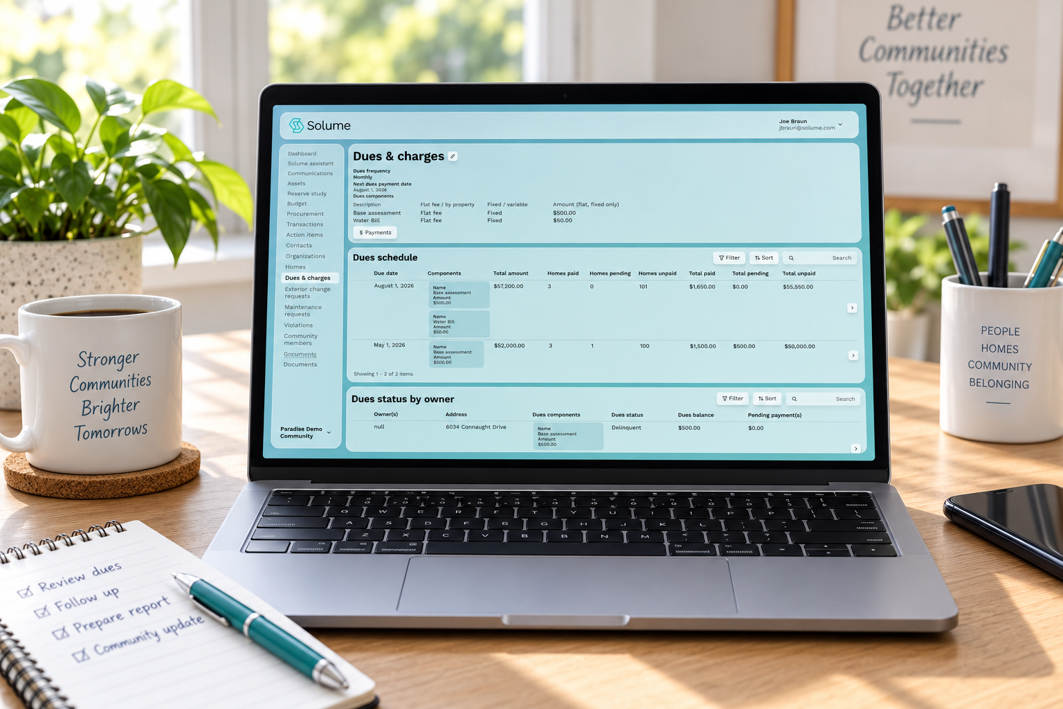 Laptop displaying a Solume HOA dues and charges dashboard with payment schedules, dues status, and financial details on a bright home-office desk.