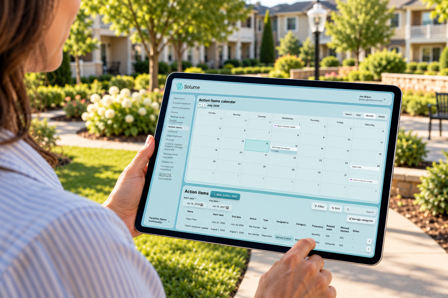 Board member using a tablet displaying Solume’s action items calendar and task dashboard in a landscaped HOA community courtyard.