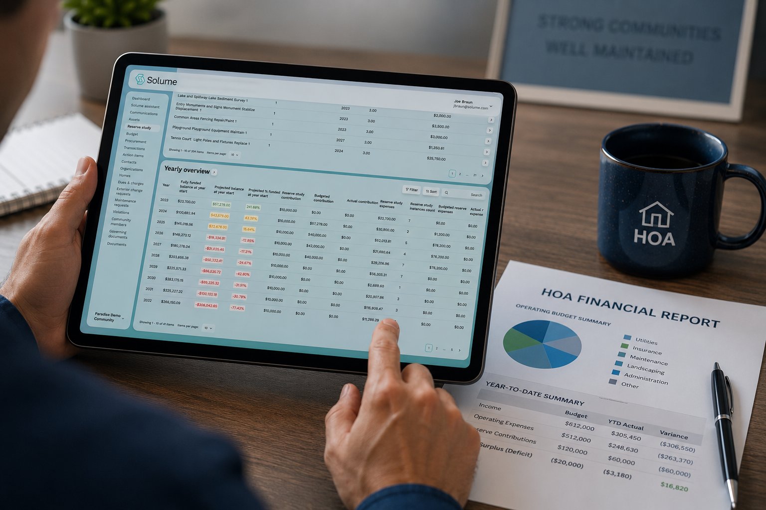 Over-the-shoulder view of a person using a tablet displaying the Solume reserve study dashboard with funding projections and financial data, alongside a printed HOA financial report and coffee mug on a wooden desk.