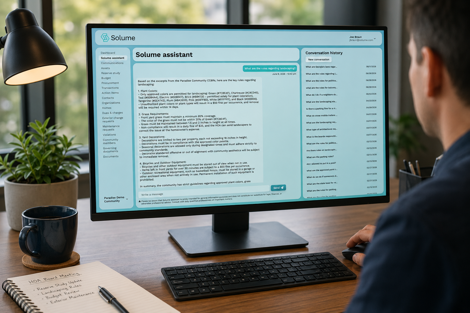 Board member viewing the Solume Assistant dashboard on a desktop monitor, displaying HOA governing document guidance and conversation history in a modern office workspace.