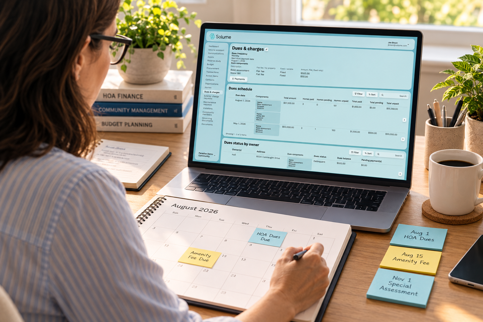 HOA treasurer reviewing the Solume Dues & Charges dashboard on a laptop while checking a calendar and tracking upcoming community dues payments at a home office desk.