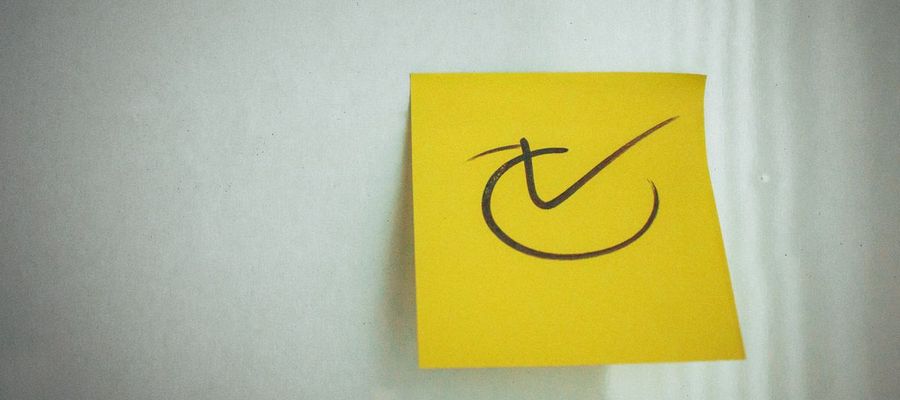 A yellow sticky note with a check mark on a white surface.