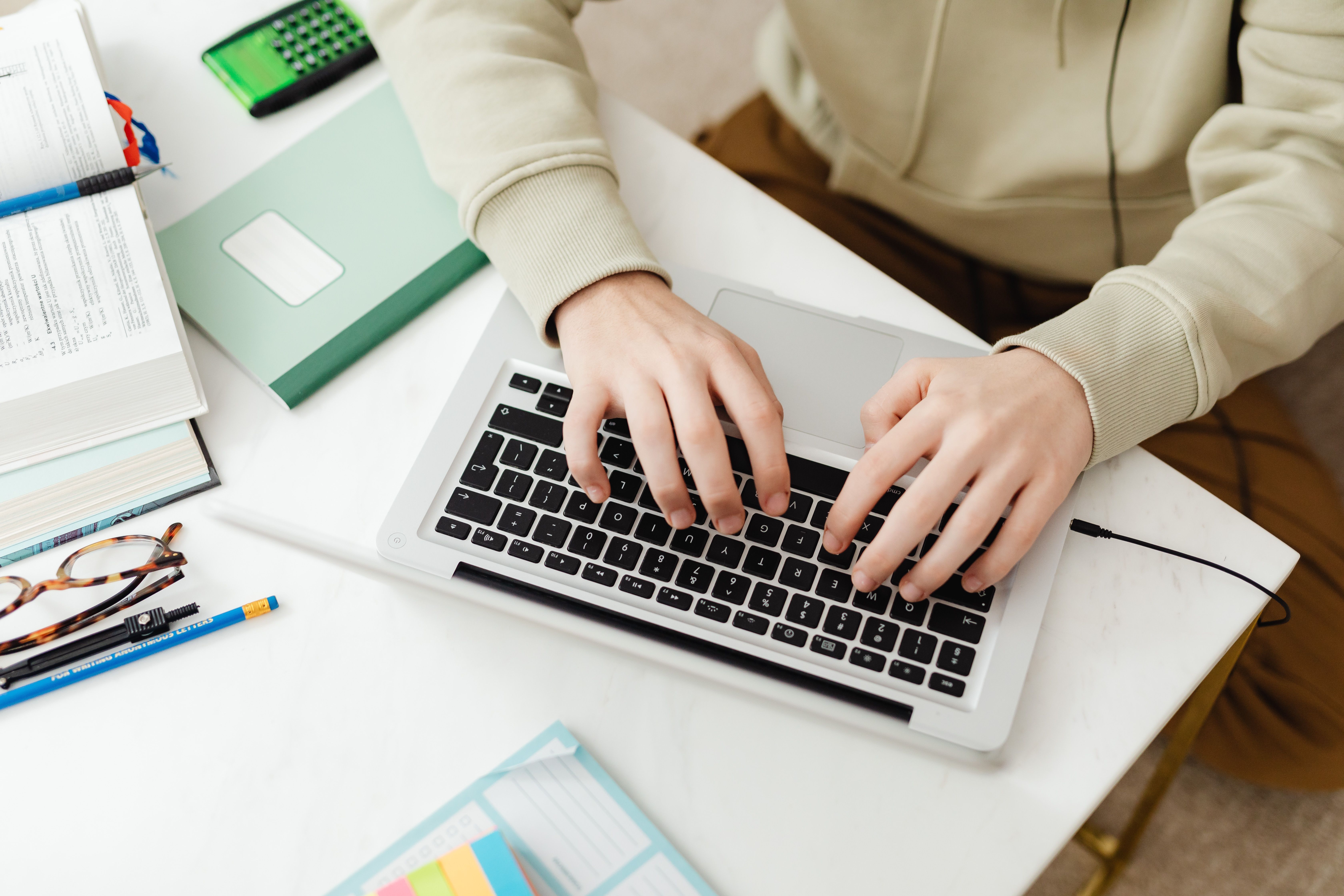 Hands typing on a laptop at a desk with study materials.