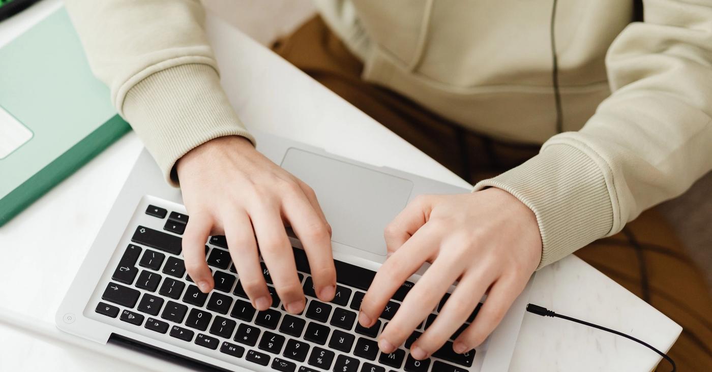 Hands typing on a laptop at a desk with study materials.