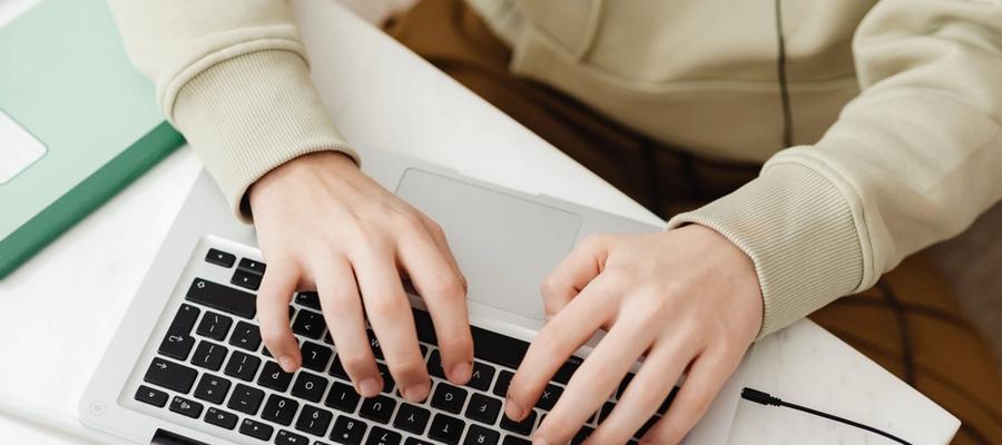 Hands typing on a laptop at a desk with study materials.