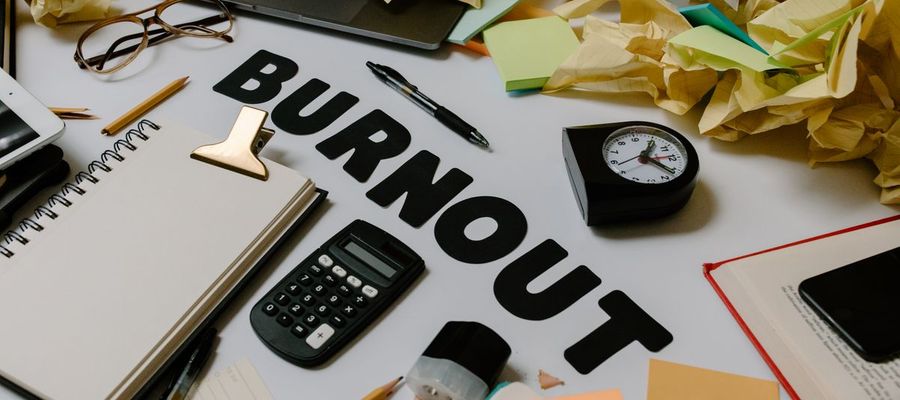 A clock, calculator and crumpled papers on a cluttered desk.