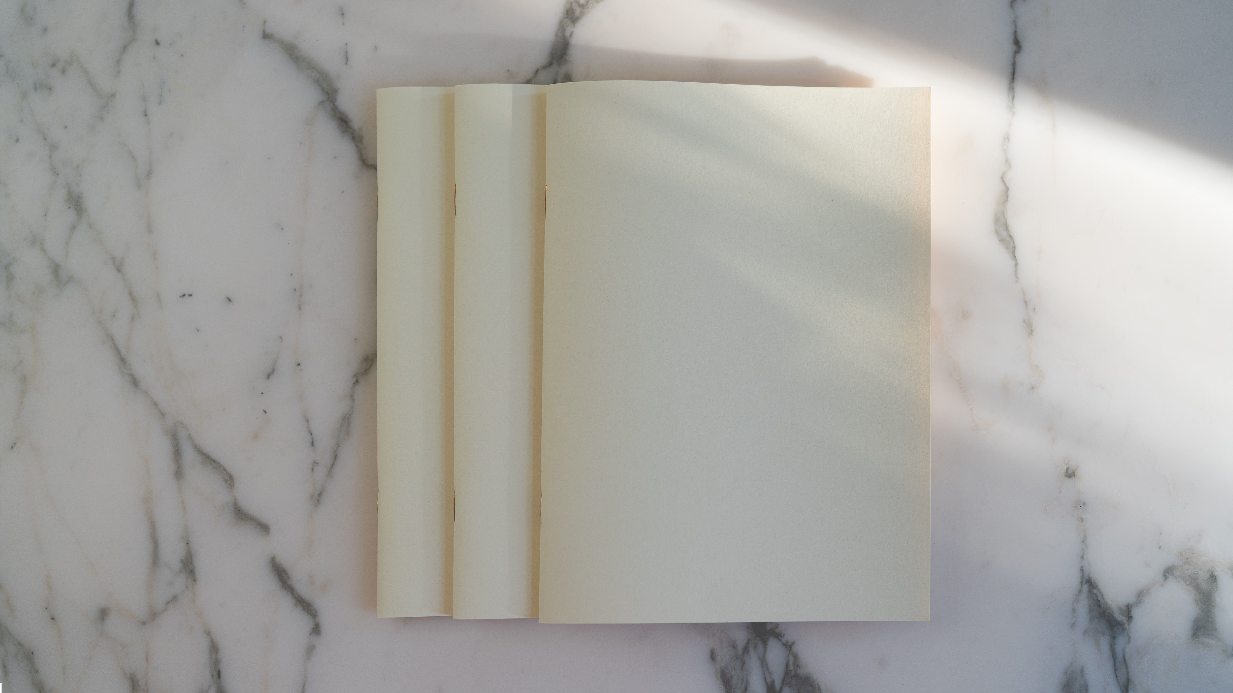 Blank cream pages on a marble surface in soft sunlight.