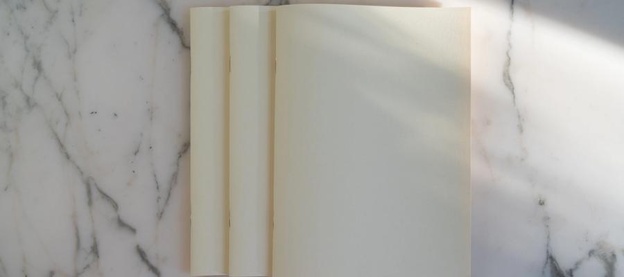 Blank cream pages on a marble surface in soft sunlight.