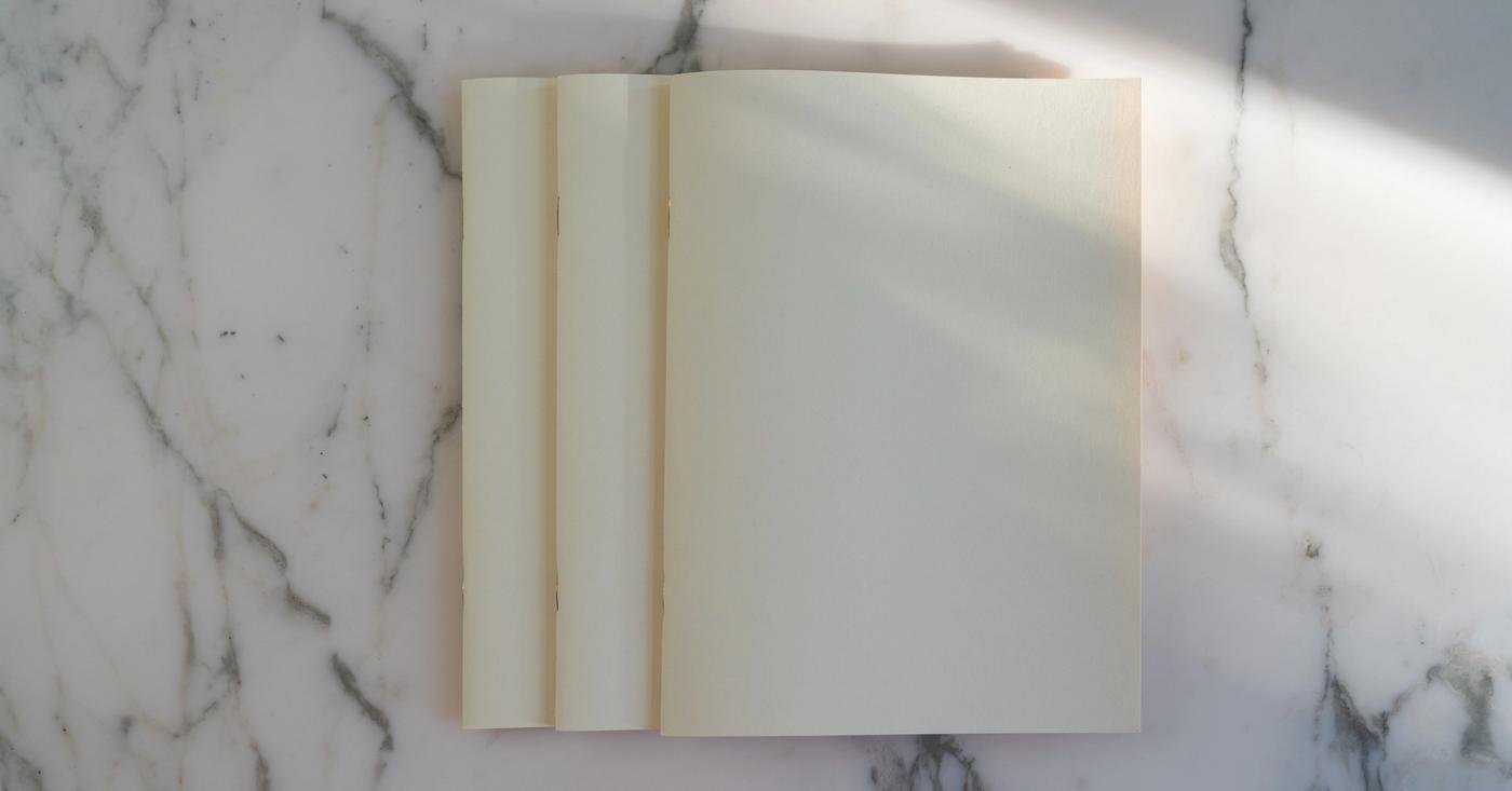Blank cream pages on a marble surface in soft sunlight.