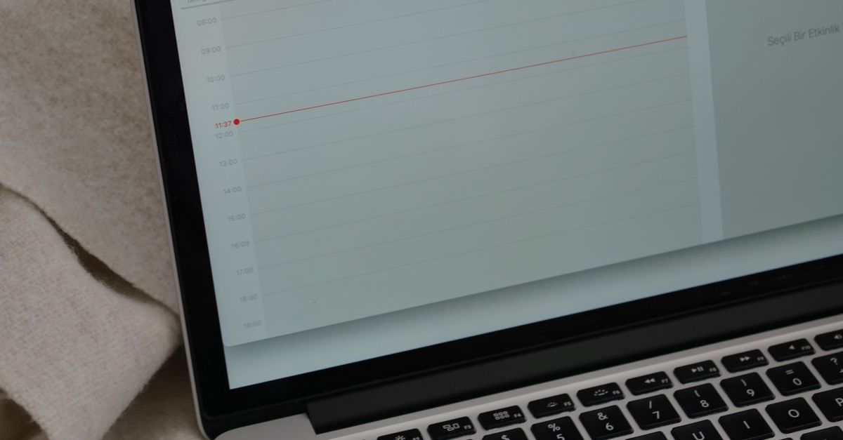 A laptop displaying a calendar beside a coffee mug on a blanket.
