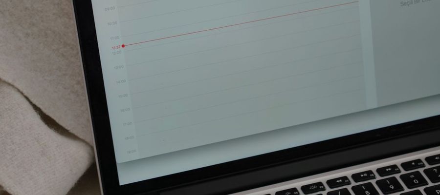 A laptop displaying a calendar beside a coffee mug on a blanket.
