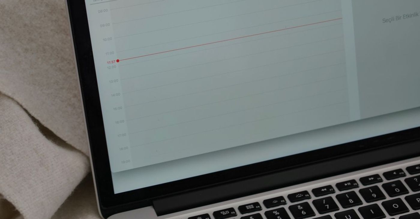 A laptop displaying a calendar beside a coffee mug on a blanket.