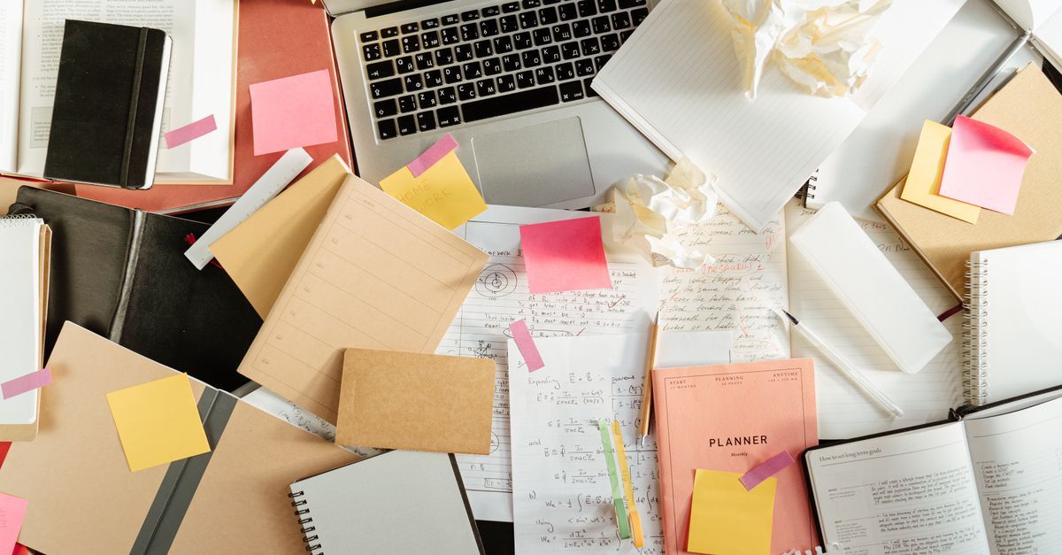 Notebooks, sticky notes and crumpled paper around a laptop on a study desk.
