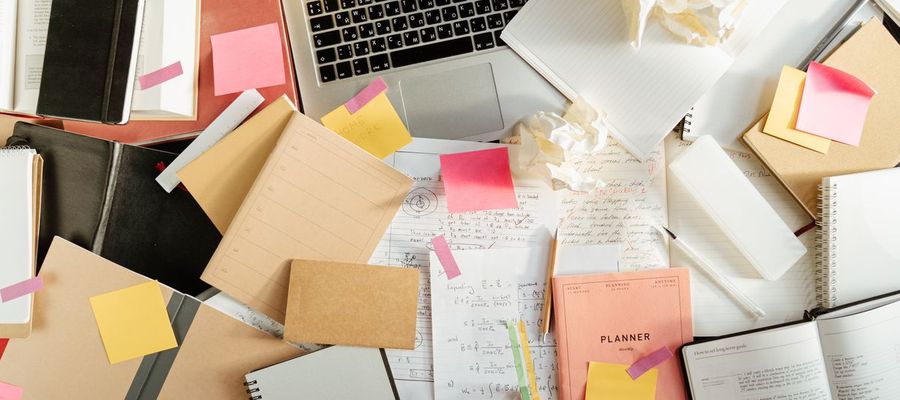 Notebooks, sticky notes and crumpled paper around a laptop on a study desk.