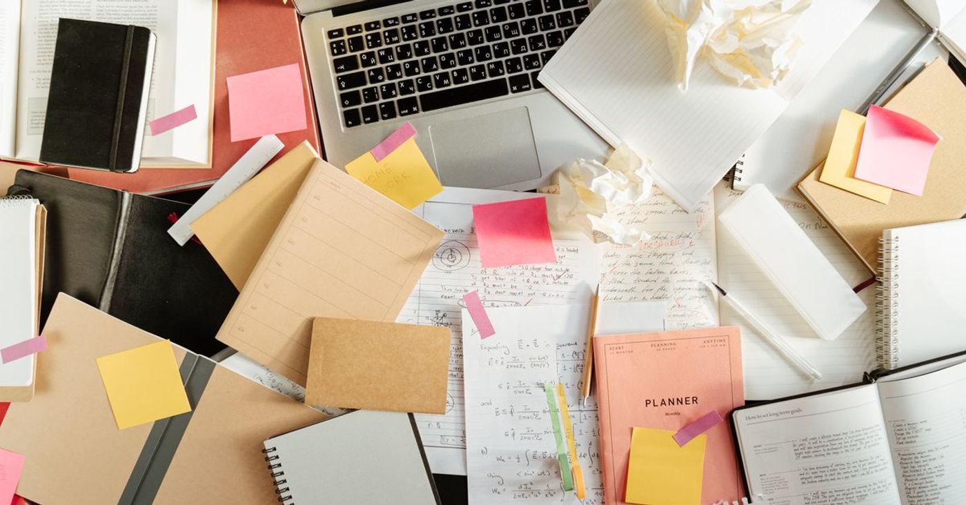 Notebooks, sticky notes and crumpled paper around a laptop on a study desk.
