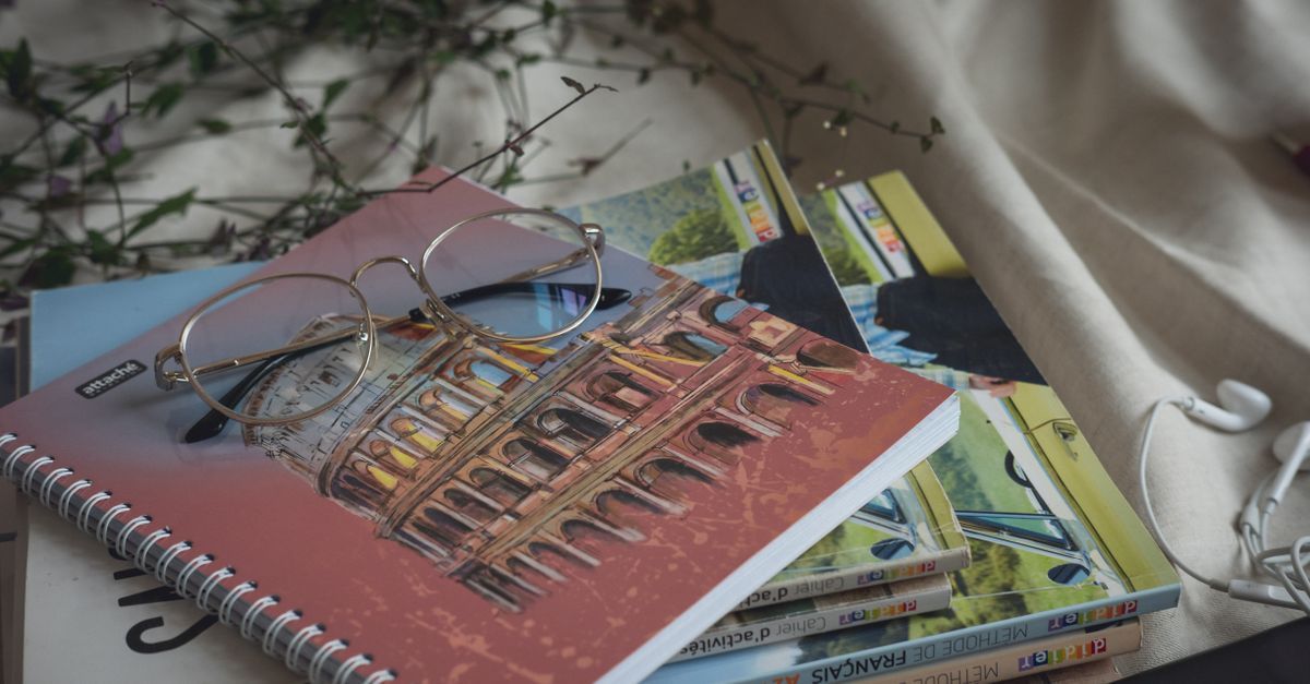 Eyeglasses rest on books and notebooks in daylight.
