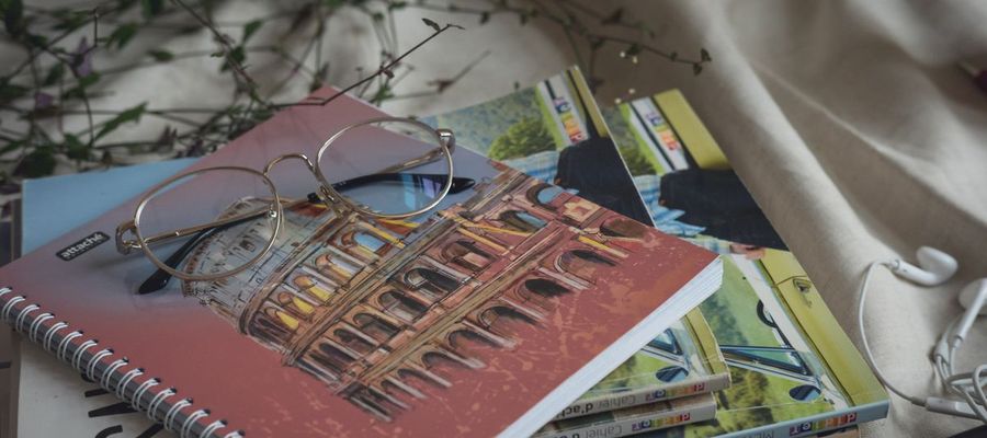 Eyeglasses rest on books and notebooks in daylight.