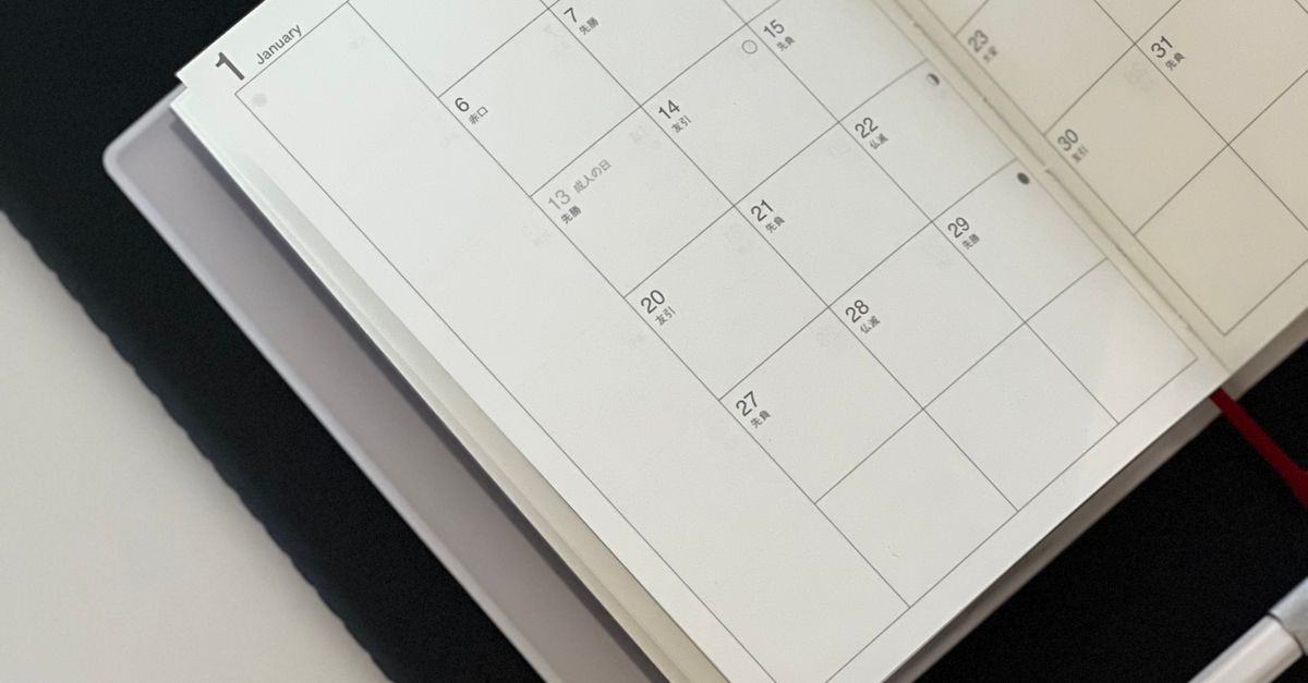 An open calendar planner with a pen and tablet on a desk.