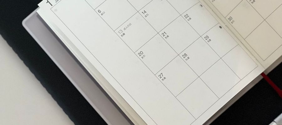 An open calendar planner with a pen and tablet on a desk.