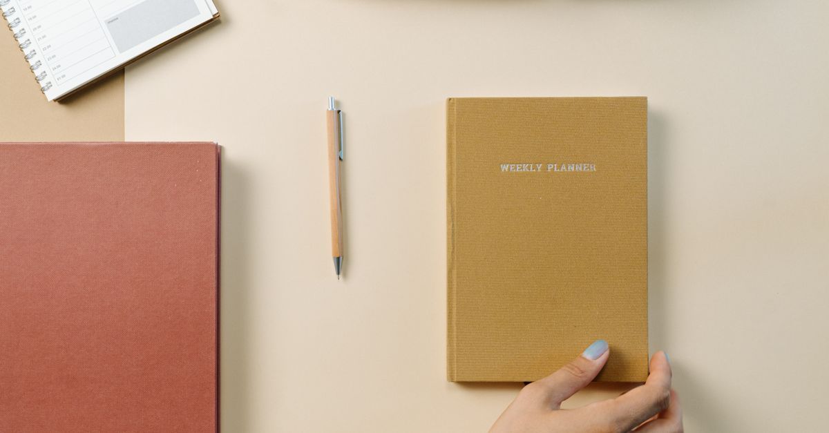 A weekly planner, notebook and pen arranged on a desk.