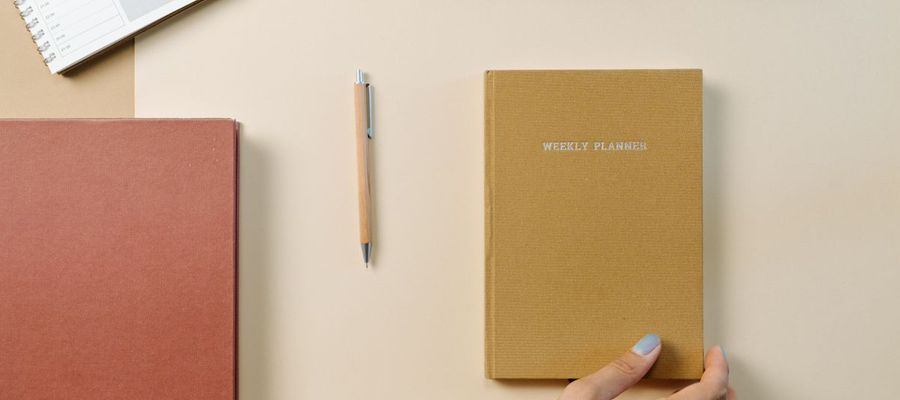 A weekly planner, notebook and pen arranged on a desk.