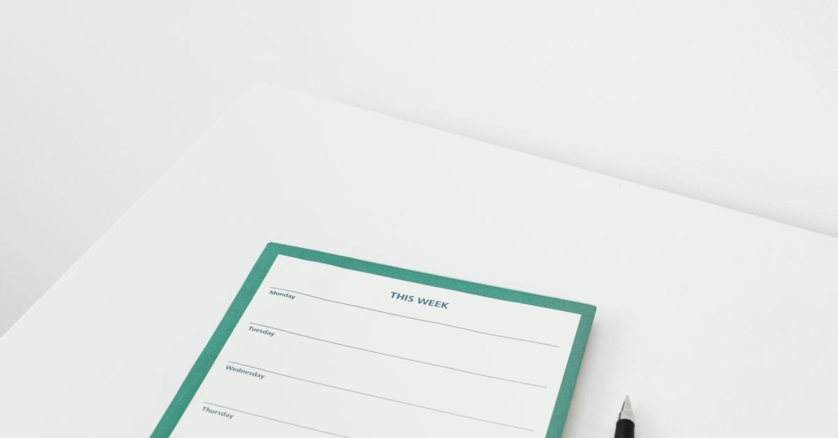 A weekly planner and black pen on a white desk.