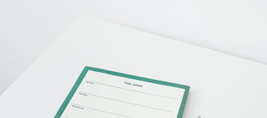 A weekly planner and black pen on a white desk.