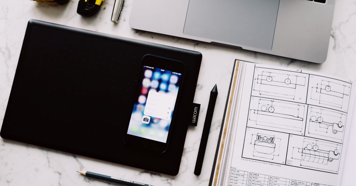 A laptop, tablet, phone and open notebook arranged on a marble table.