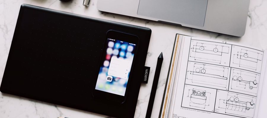 A laptop, tablet, phone and open notebook arranged on a marble table.