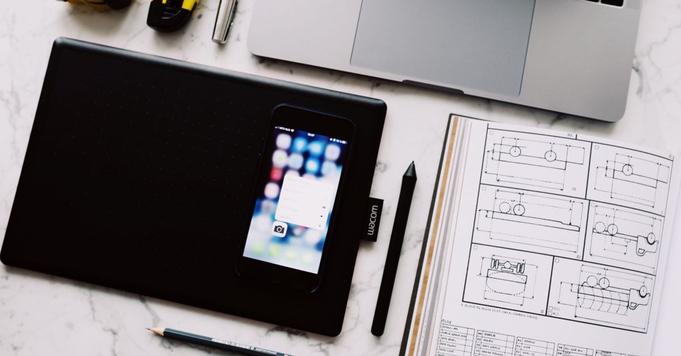 A laptop, tablet, phone and open notebook arranged on a marble table.
