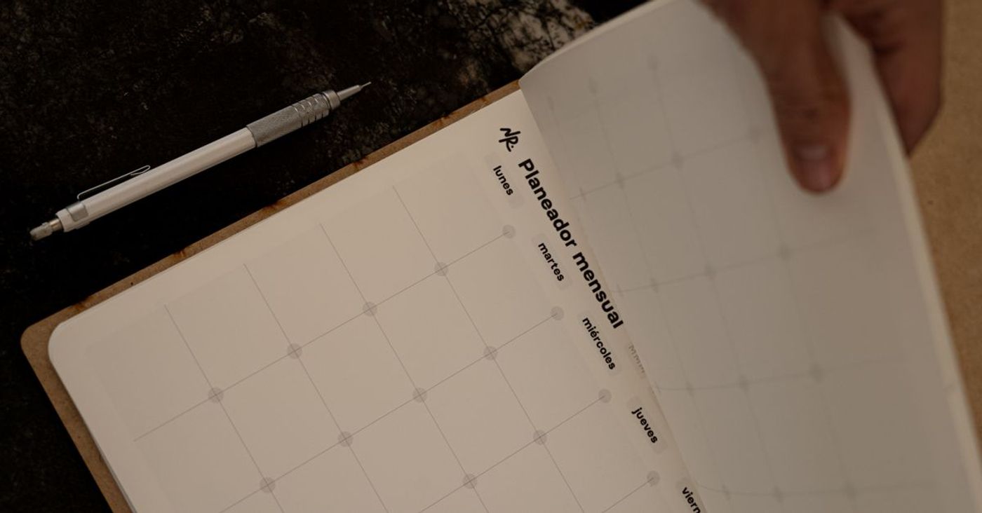 Hands turn a page in a monthly planner with a pen nearby.