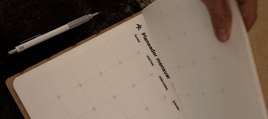 Hands turn a page in a monthly planner with a pen nearby.
