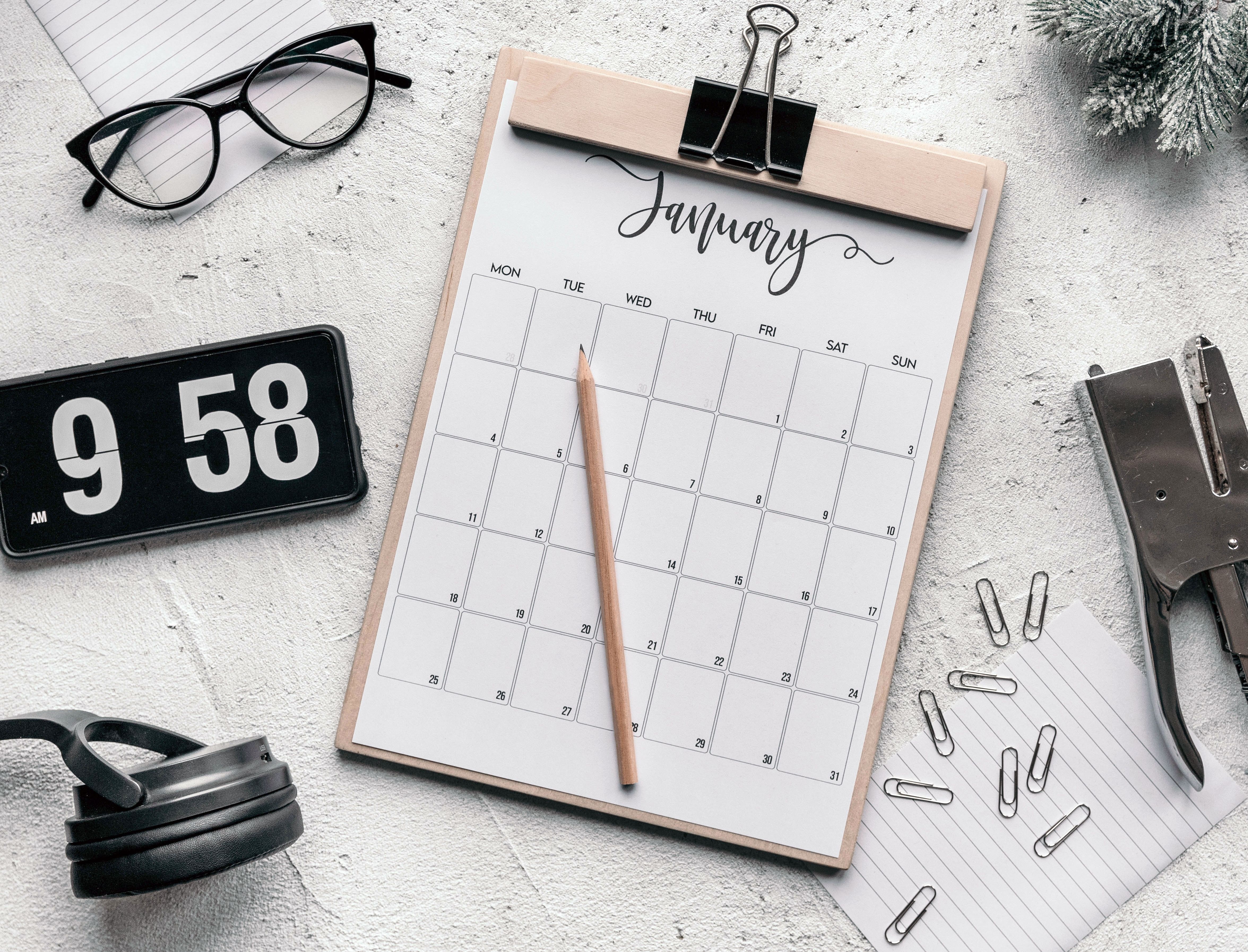 Calendar sheet on a clipboard beside a flip clock and stationery.