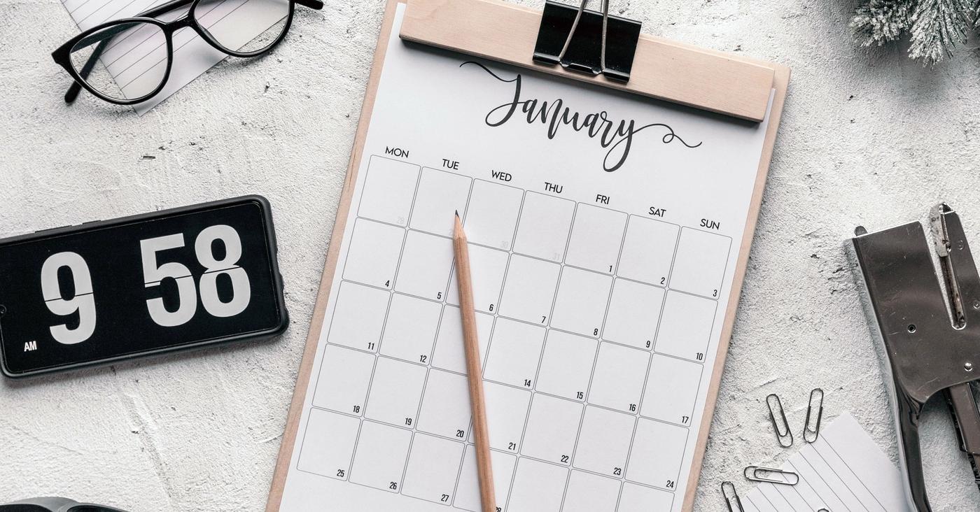 Calendar sheet on a clipboard beside a flip clock and stationery.