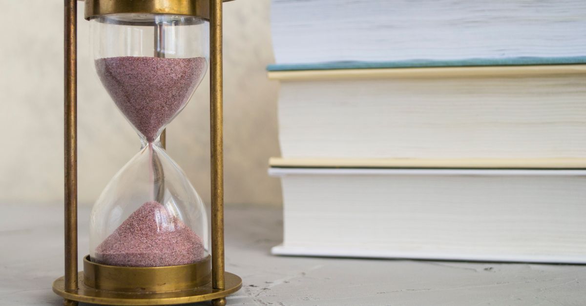 An hourglass with red sand stands beside a stack of books.