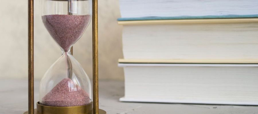 An hourglass with red sand stands beside a stack of books.