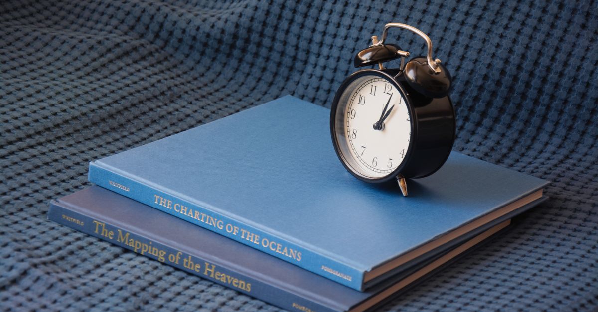 A black alarm clock sits on a stack of blue books.